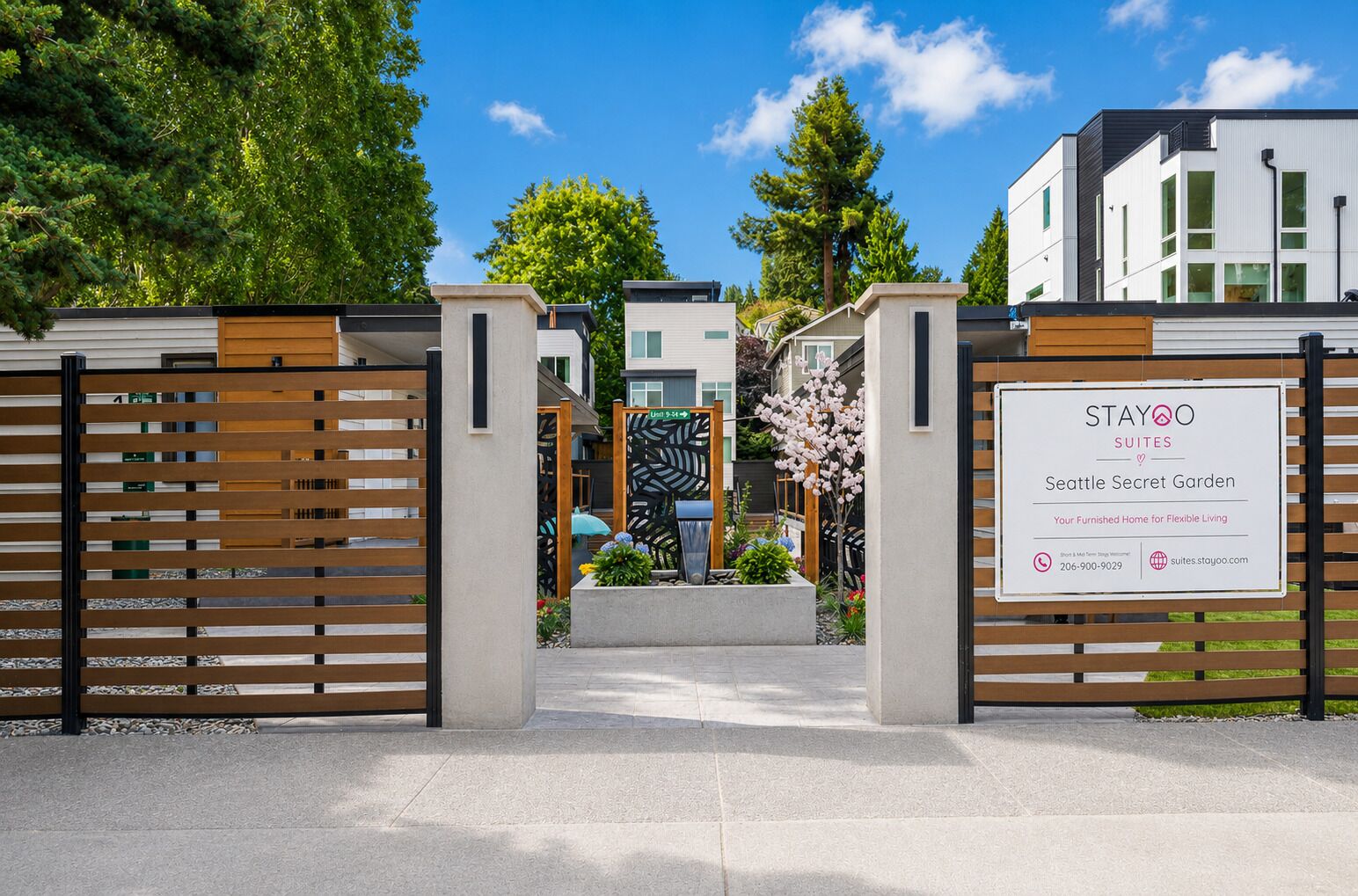 A gated entrance to a modern building with a sign for Stayoo Suites Seattle Secret Garden.