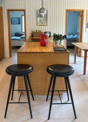 Eine moderne Küche mit einer Holztischinsel, zwei schwarzen Barhocker, einer roten Karaffe und einer hängenden Pendelleuchte.