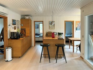 Eine moderne Küche mit Holzausstattung, einer zentralen Kochinsel mit Hockern und einem Essbereich mit Tisch und Stühlen.