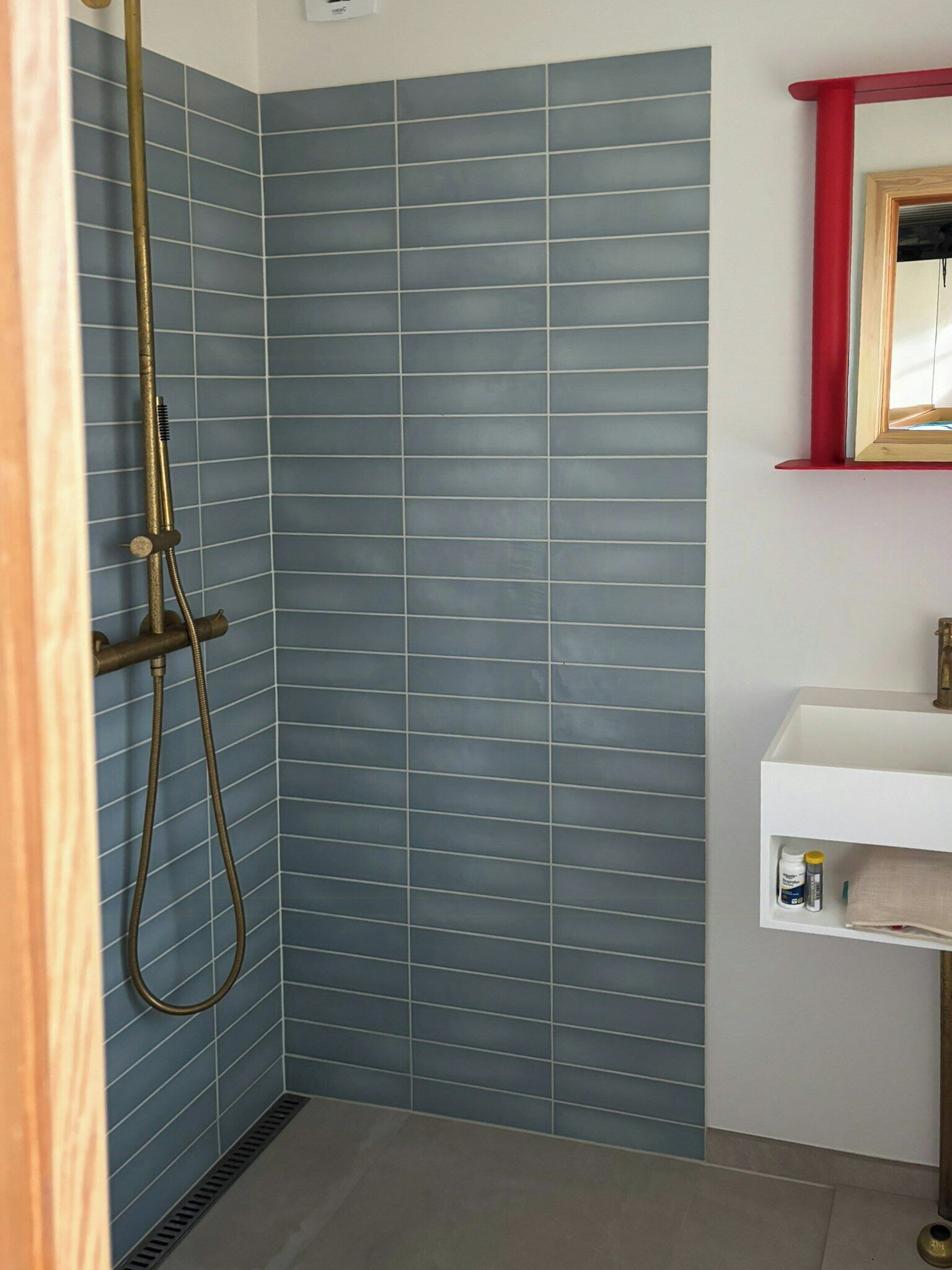 A bathroom with blue tiled walls, a shower with a gold showerhead, and a white sink with a red frame mirror.