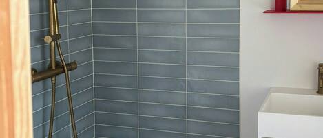 A bathroom with blue tiled walls, a shower with a gold showerhead, and a white sink with a red frame mirror.