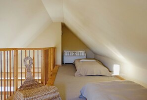 A room with a sloped ceiling, a wooden chair, two beds, and a bedside table with a lamp.