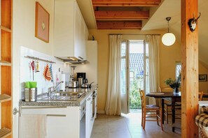 A kitchen with a sink, stove, and cabinets, a dining area with a table and chairs, and a view of the outdoors.