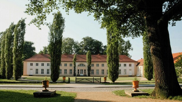 A large building with a symmetrical facade, a central entrance, and a paved pathway leading to it.