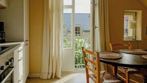 A kitchen with a dining area, a window with curtains, a lamp, and a view of a house.