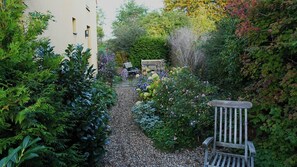 A garden pathway leading to a bench, surrounded by lush greenery and flowering plants.