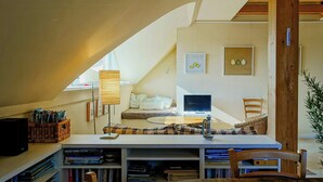 A cozy reading nook with a desk, bookshelves, a laptop, and a comfortable chair.