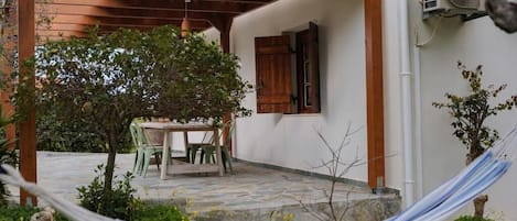 Eine überdachte Terrasse mit Tisch, Stühlen, einer Hängematte und einem kleinen Baum.