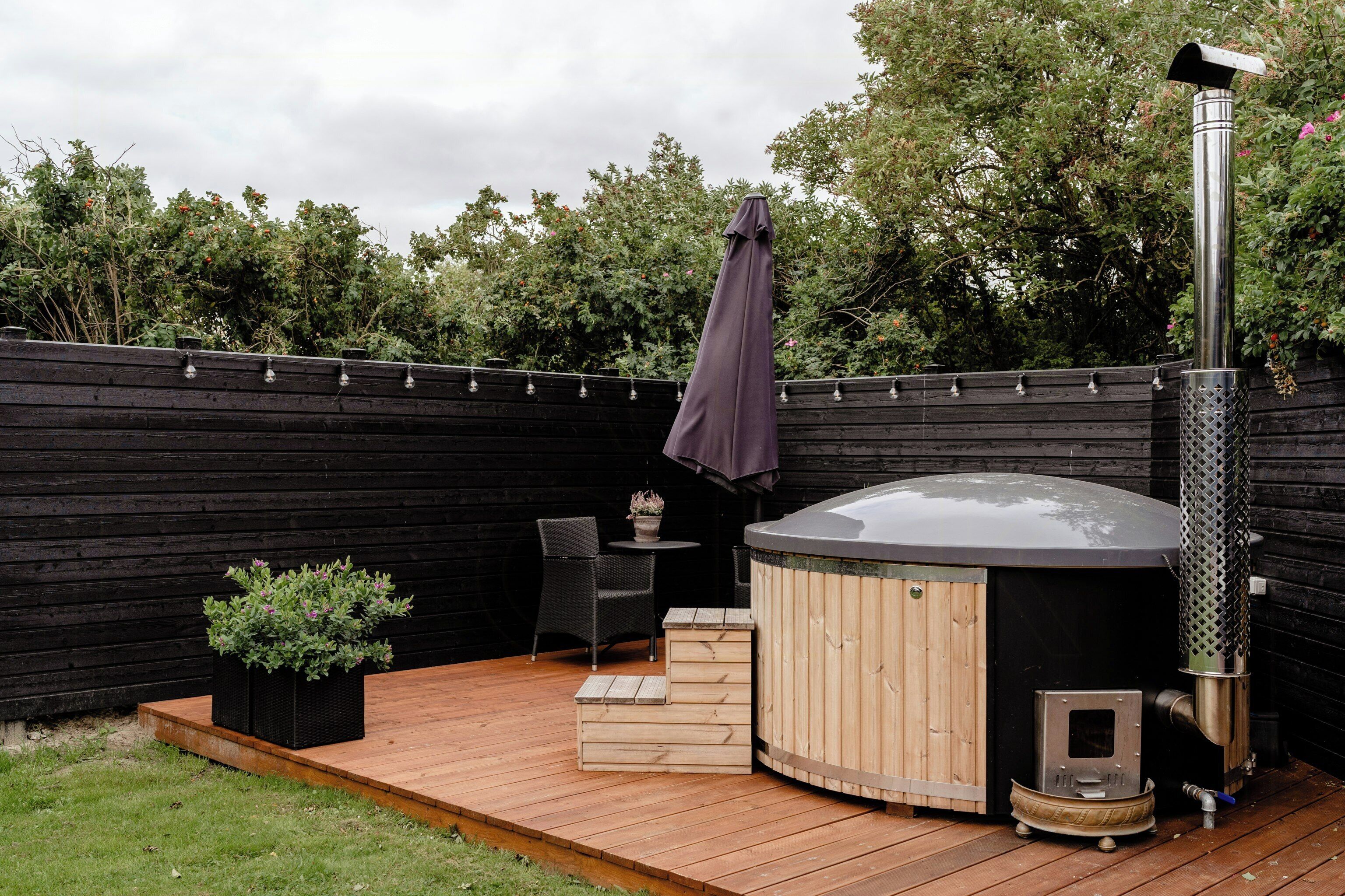 A hot tub with a wooden deck, a table with chairs, and a potted plant.