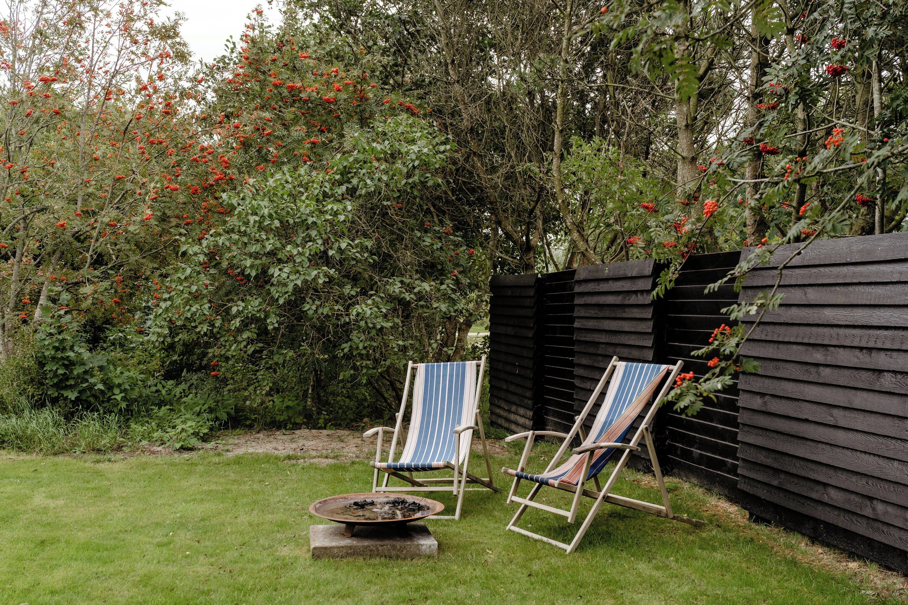 Two striped lounge chairs, a fire pit, and a wooden fence in a garden setting.