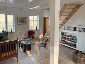 A room with a wooden floor, a fireplace, a bookshelf, and a window with a view of trees. - Renovated stone house from 1877 in Listed Bornholm (Svaneke)