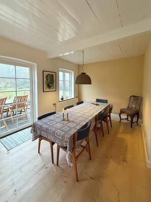 A dining area with a long table, chairs, a pendant light, and a view through a glass door. - Renovated stone house from 1877 in Listed Bornholm (Svaneke)