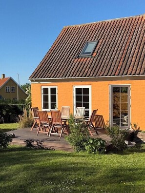 A house with a tiled roof, a small window, and a patio with chairs. - Renovated stone house from 1877 in Listed Bornholm (Svaneke)