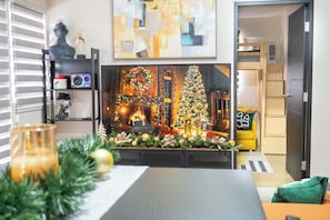 Una sala de estar con chimenea, un árbol de Navidad y una obra de arte moderno en la pared de arriba.