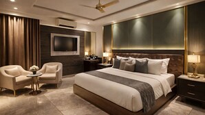 A modern hotel room with a large bed, a TV, a ceiling fan, and a seating area with two chairs. - NH Skye Suites Hotel  (New Delhi)