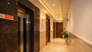 A hotel corridor with marble flooring, a no smoking sign, an elevator, and potted plants. - NH Skye Suites Hotel  (New Delhi)
