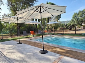 Ein Swimmingpool mit zwei Sonnenschirmen, umgeben von Stühlen und einem Zaun.