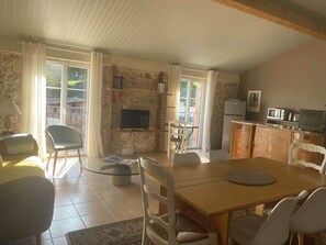 Ein gemütliches Wohnzimmer mit Fernseher, Esstisch, Stühlen und einer Küchenzeile mit Geräten.