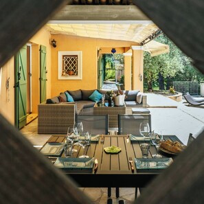 Ein Sitzbereich im Freien mit einer Couch, einem Esstisch und Stühlen, einer Topfpflanze und Blick auf den Garten.