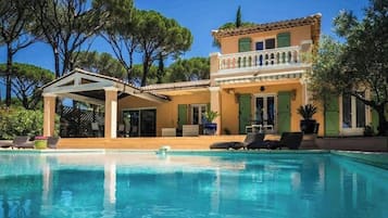 Une maison à deux étages dotée d’une piscine, d’un espace salon extérieur et d’une terrasse couverte.