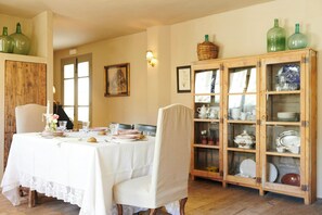 Une salle à manger avec une table dressée pour quatre personnes, des chaises, un buffet aux portes vitrées et un tableau accroché au mur.