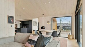 A modern interior with a sofa, dining table, chairs, and a large window. - Summer house by Mols Bjerge Trail with sea view (Knebel)