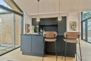 Ett modernt kök med en svart köksö, två barstolar, hängande lampor och ett stort fönster.