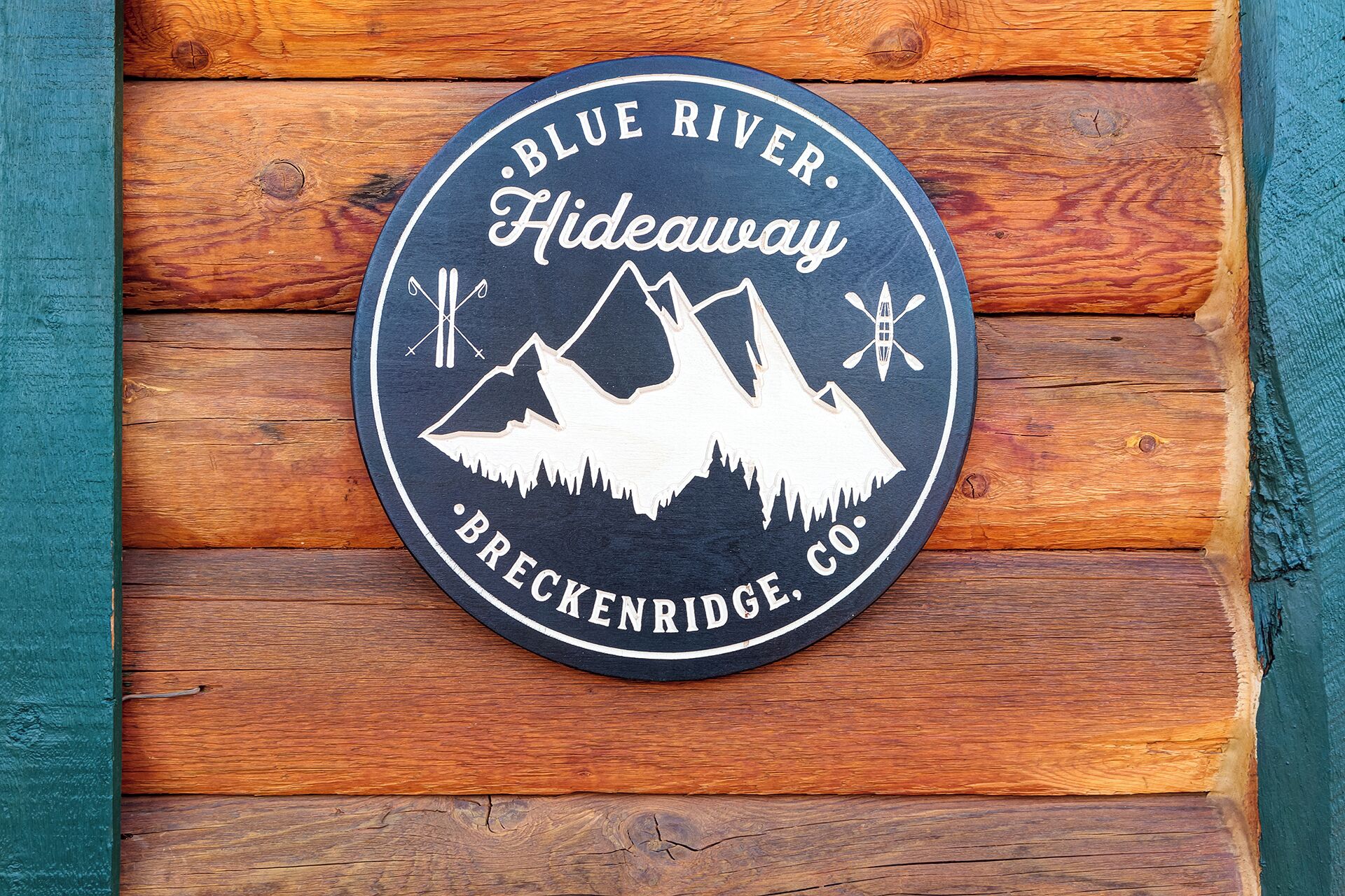 Pyöreä kyltti, jossa lukee tekstiä «Blue River Hideaway» ja «Brecknridge, CO», ja jossa on kuvia vuorista ja melontalautoista.