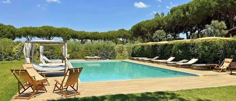 A rectangular swimming pool with a wooden deck, surrounded by lounge chairs and a canopy structure.