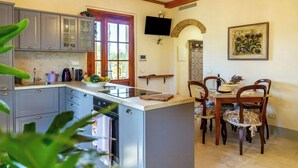 A kitchen with a central island, grey cabinets, a built-in dishwasher, and a dining area with a wooden table and chairs. - Private villa among pine trees and lavender (Marina Di Grosseto)
