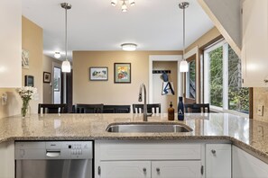 Una cocina moderna con lavavajillas Bosch, encimeras de granito, pileta de acero inoxidable, luces colgantes y obras de arte en las paredes.