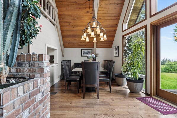 Un espace repas doté d’un plafond en bois, d’un lustre et offrant une vue sur l’extérieur.