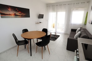 Ein Wohnzimmer mit einem runden Tisch, schwarzen Stühlen, einer Couch, einem Fernseher und einem Sonnenuntergangsbild.