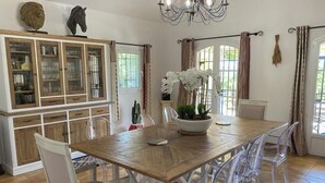 A dining area with a wooden table, clear chairs, a chandelier, and a cabinet with glass doors.
