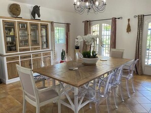 A dining area with a wooden table, clear chairs, a chandelier, and a cabinet with glass doors. - Provençal mansion in the heart of Luberon (Murs)