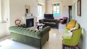 Un saló amb una llar de foc, sofàs verdosos, un piano i un butac armchair verd.