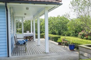Eine überdachte Veranda mit Tisch und Stühlen, eine Bank sowie ein Garten mit Hecke und Blumentöpfen.