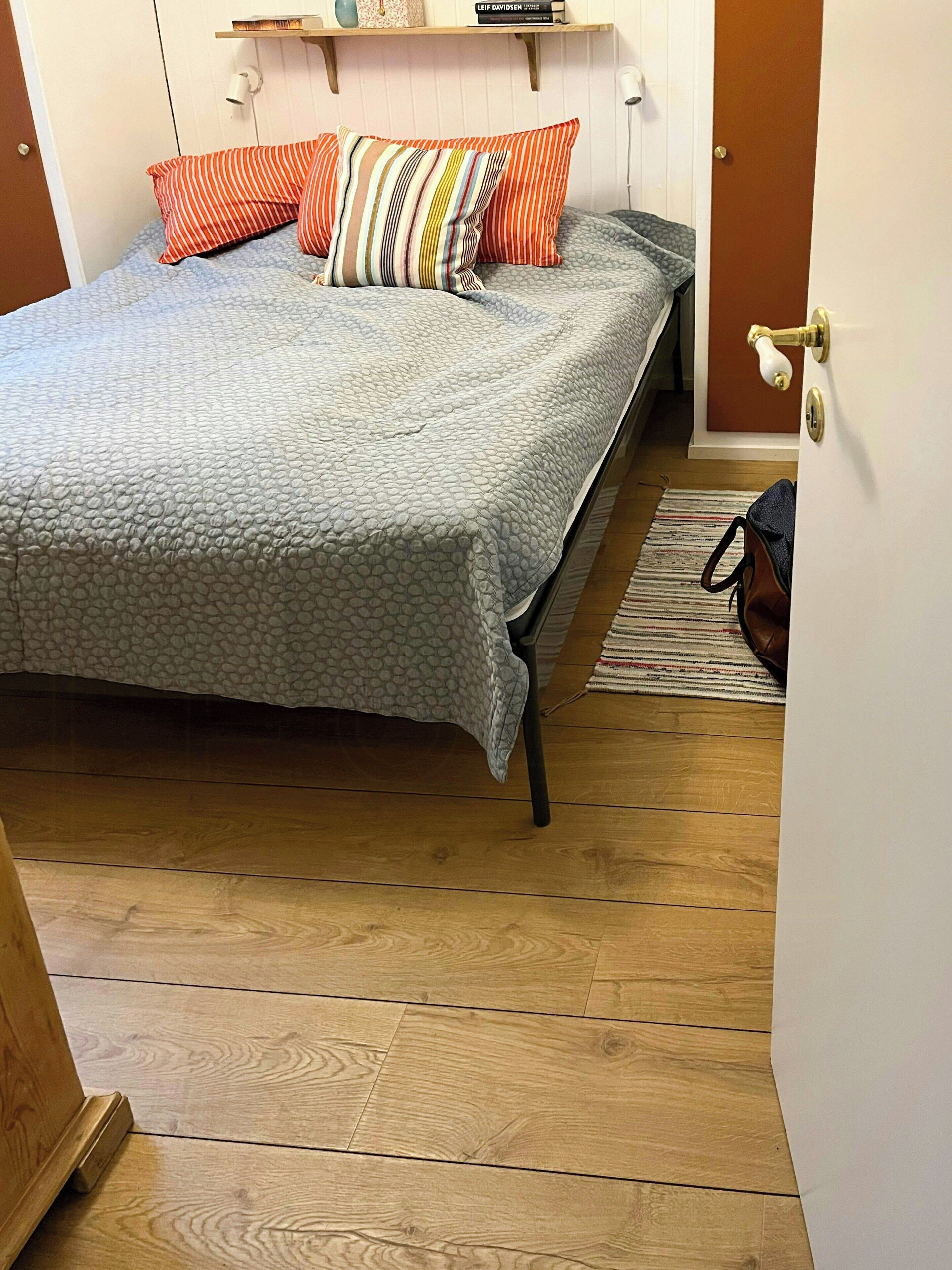 A bed with a patterned bedspread, striped pillows, and a wooden floor.