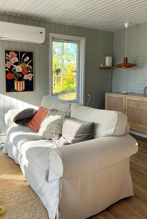 Ein Wohnzimmer mit einem weißen Sofa, einem Blumenbild, einem Fenster und einem Holzschrank.