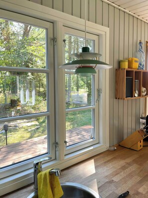 Eine Küche mit großem Fenster, einer Pendelleuchte, einem Holzschrank und einem Spülbecken.