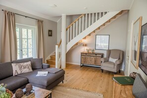 A living room with a sofa, a chair, a staircase, and a wooden floor. - Forestry chic: flat with lake and forest view (Friedeburg)