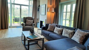 A living room with a sofa, armchair, coffee table, and a fireplace. - Forestry chic: flat with lake and forest view (Friedeburg)