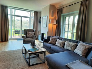 A living room with a sofa, armchair, coffee table, and a fireplace. - Forestry chic: flat with lake and forest view (Friedeburg)