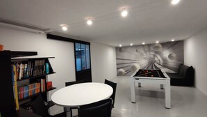 Quarto com mesa de bilhar, mesa redonda branca e estantes.