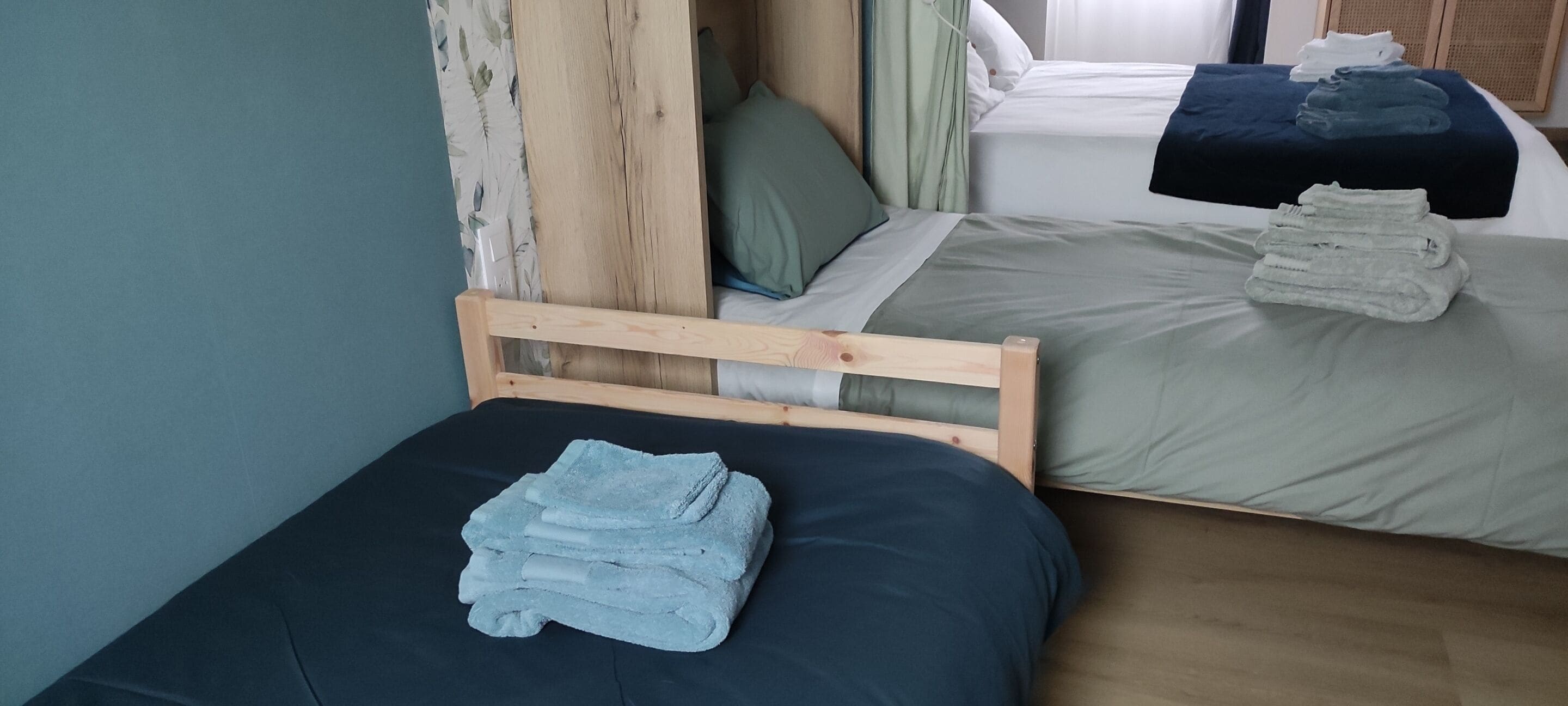 Quarto com duas camas, uma com cabeceira de madeira e outra sem adornos. Toalhas em ambas as camas.