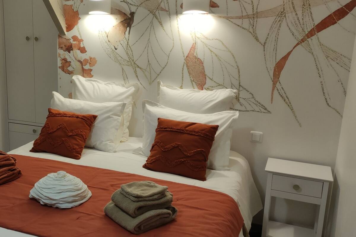 Una cama bien hecha con una colcha roja, dos almohadas y toallas dobladas.