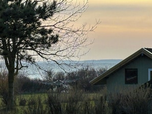 Ein Haus mit geneigtem Dach, umgeben von Bäumen und einem Feld.