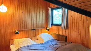 Een kamer met houten lambrisering, een bed, twee bedlampen en een raam met gordijnen.