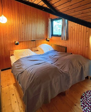 Una habitación con paneles de madera, una cama, dos lámparas de noche y un ventanal con cortinas.
