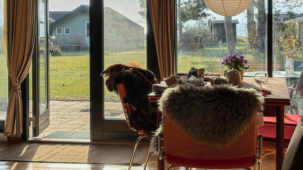 Een kamer met een grote schuifdeur, een fauteuil met een bont plaid, een tafel met een bloevas en een hangende papieren lantaarn.